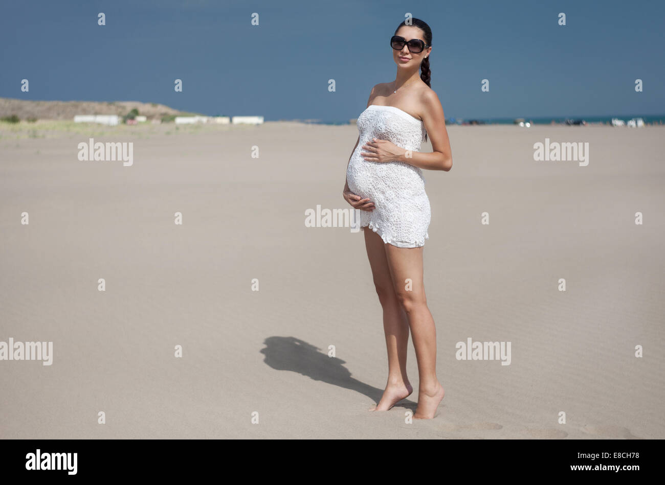 Donna incinta in bikini bianco in posa sulla spiaggia Foto Stock