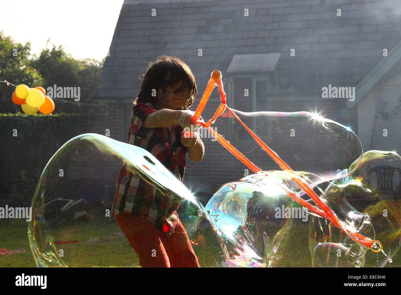 Un giovane bambino rendendo le bolle in un giardino in una giornata d'estate durante una festa in giardino. Foto Stock