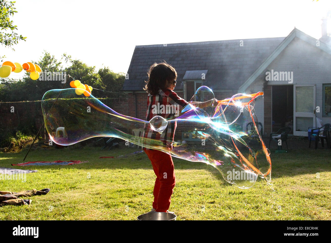 Un giovane bambino rendendo le bolle in un giardino in una giornata d'estate durante una festa in giardino. Foto Stock