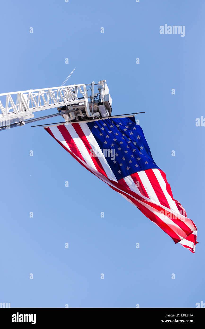 Una bandiera americana sta volando da un esteso reparto antincendio scaletta / antenna su un cielo blu chiaro giorno Foto Stock