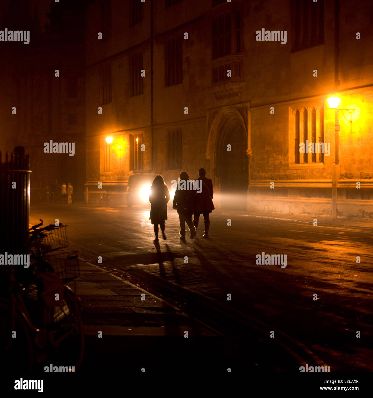 Scena notturna nel centro storico di Oxford. 3 studenti a piedi, vecchia biblioteca Bodleian, Radcliffe Camera .Bikes in silhouette in primo piano Foto Stock