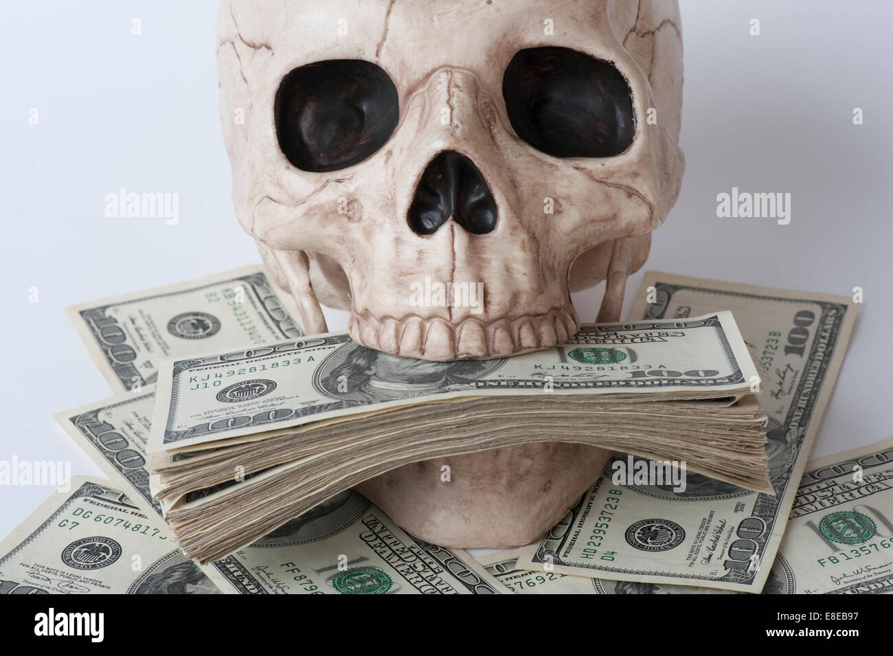 Cranio umano circondato da pile di banconote da cento dollari concetto avidità Foto Stock