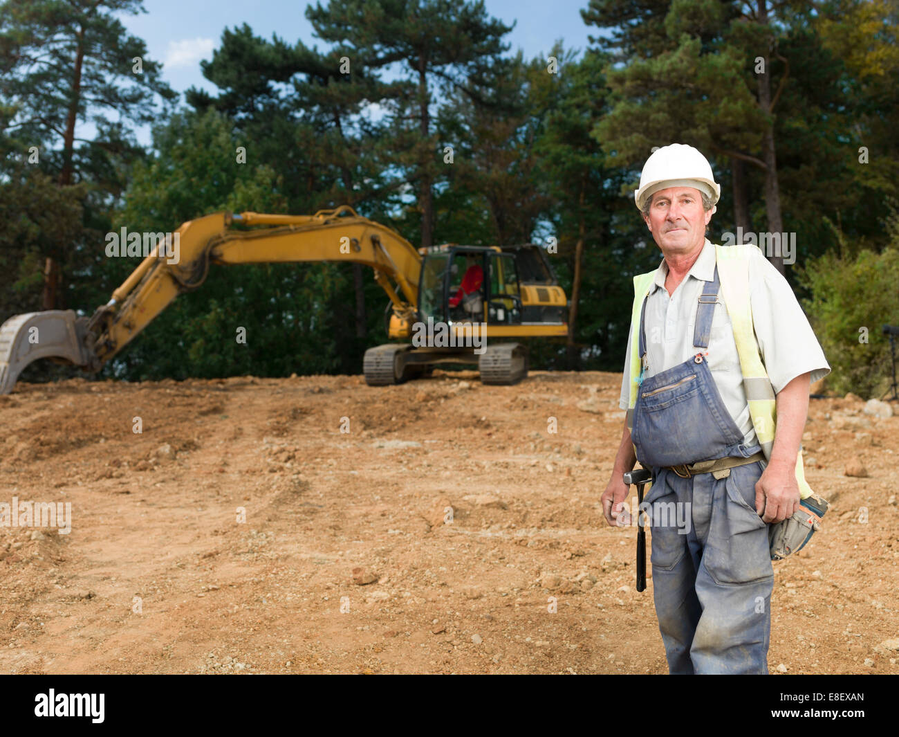 Ritratto di senior operaio in uniforme blu sul sito in costruzione all'aperto Foto Stock