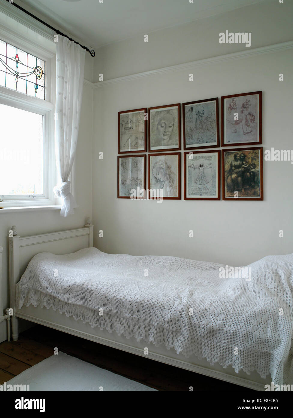 Collezione di cornici e disegni sopra un letto singolo con pizzo bianco cover letto in bianco camera per gli ospiti Foto Stock