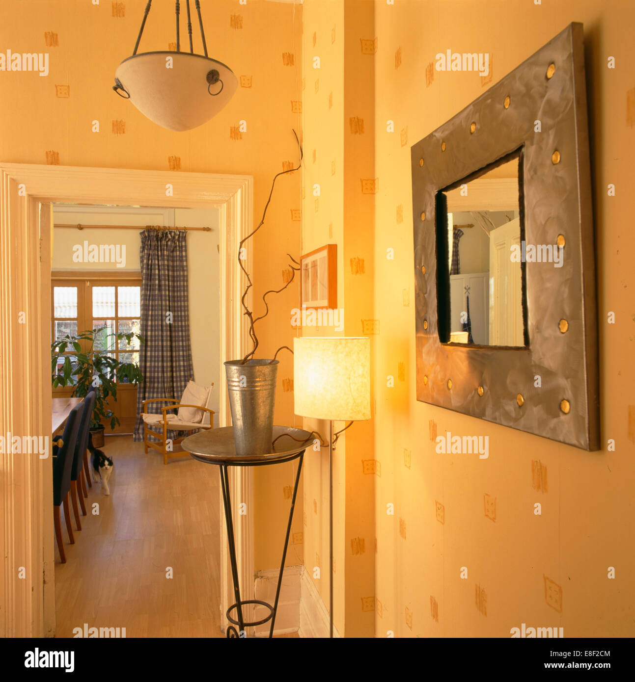 Metallo specchio incorniciato e pianta stand in piccola e moderna hall con la lampada accesa e pareti decorate con un motivo stampato Foto Stock