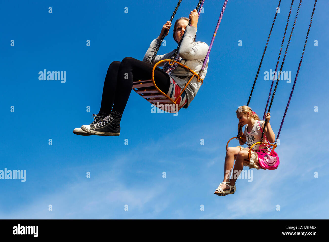 Adolescenti, due ragazze sulla catena swing carosello cavalcare cielo blu Foto Stock