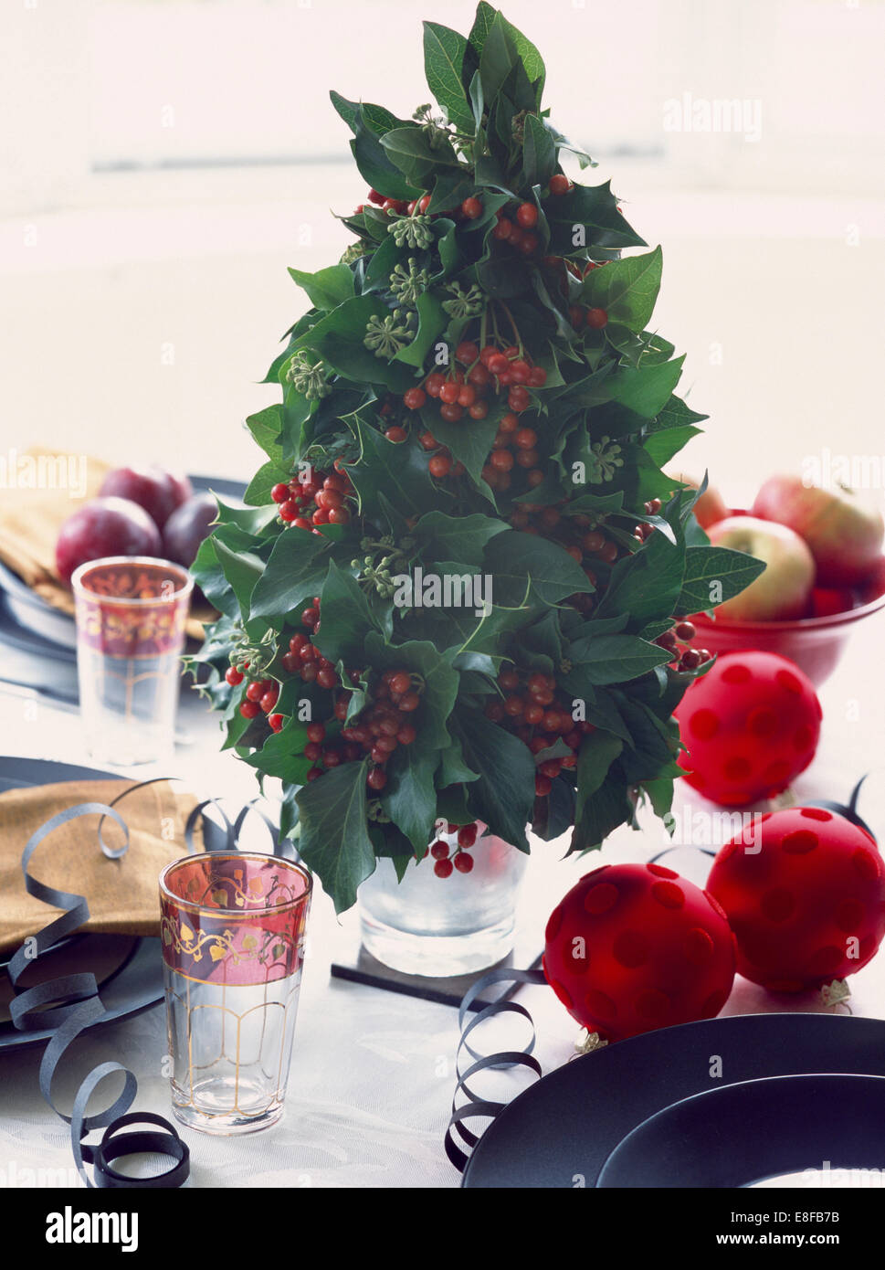 Close-up di Natale Decorazioni per la tavola di piccolo albero realizzato da foglie d'edera e bacche di agrifoglio Foto Stock