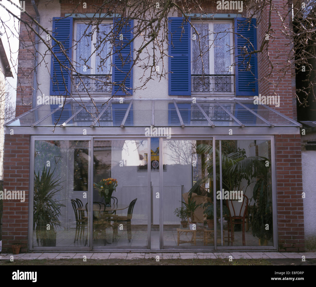 Porte di vetro scorrevoli sulla moderna serra interno sul tradizionale casa cittadina francese con persiane blu Foto Stock