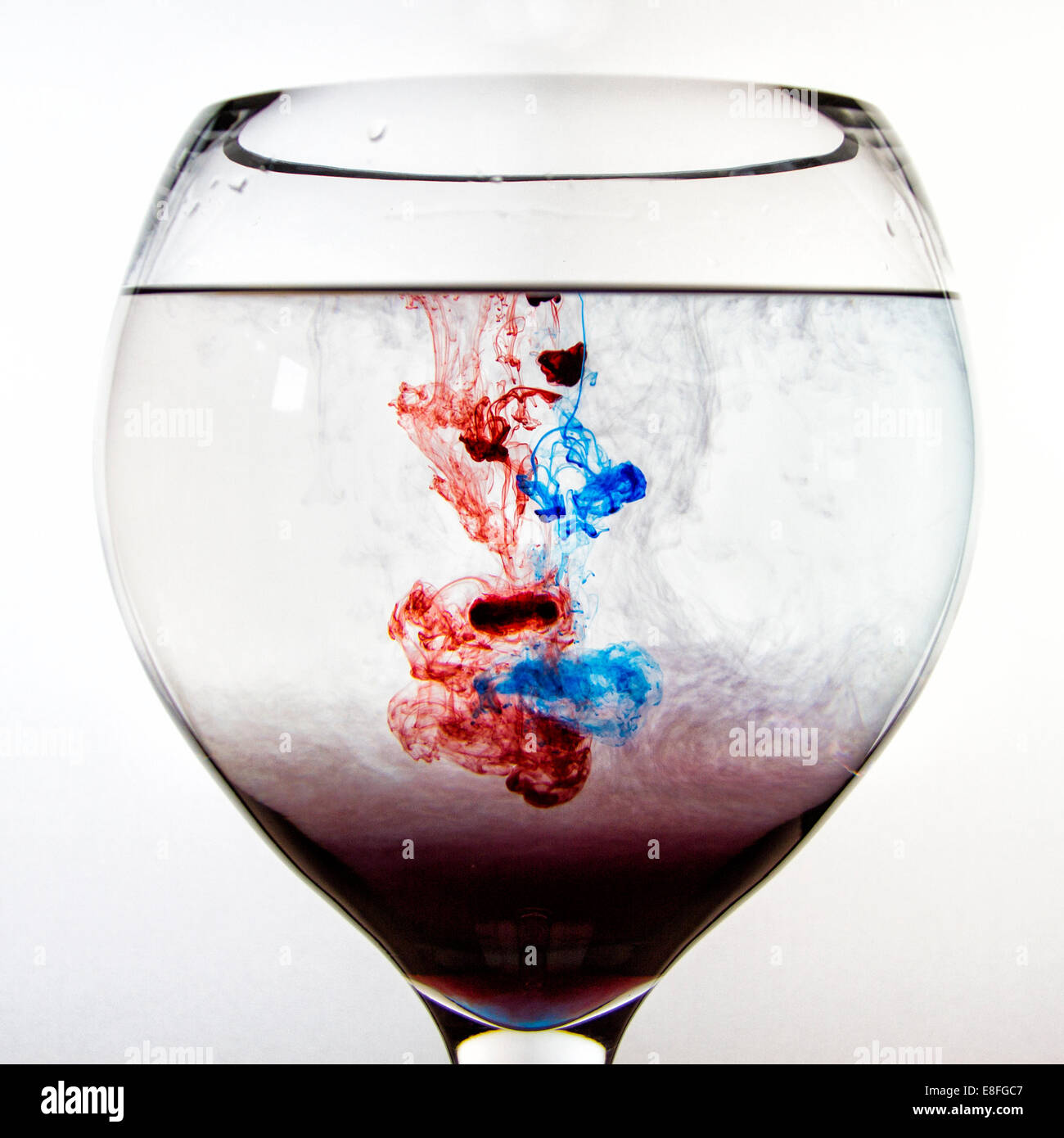 Il rosso e il blu inchiostro sciogliere in un bicchiere di acqua Foto Stock