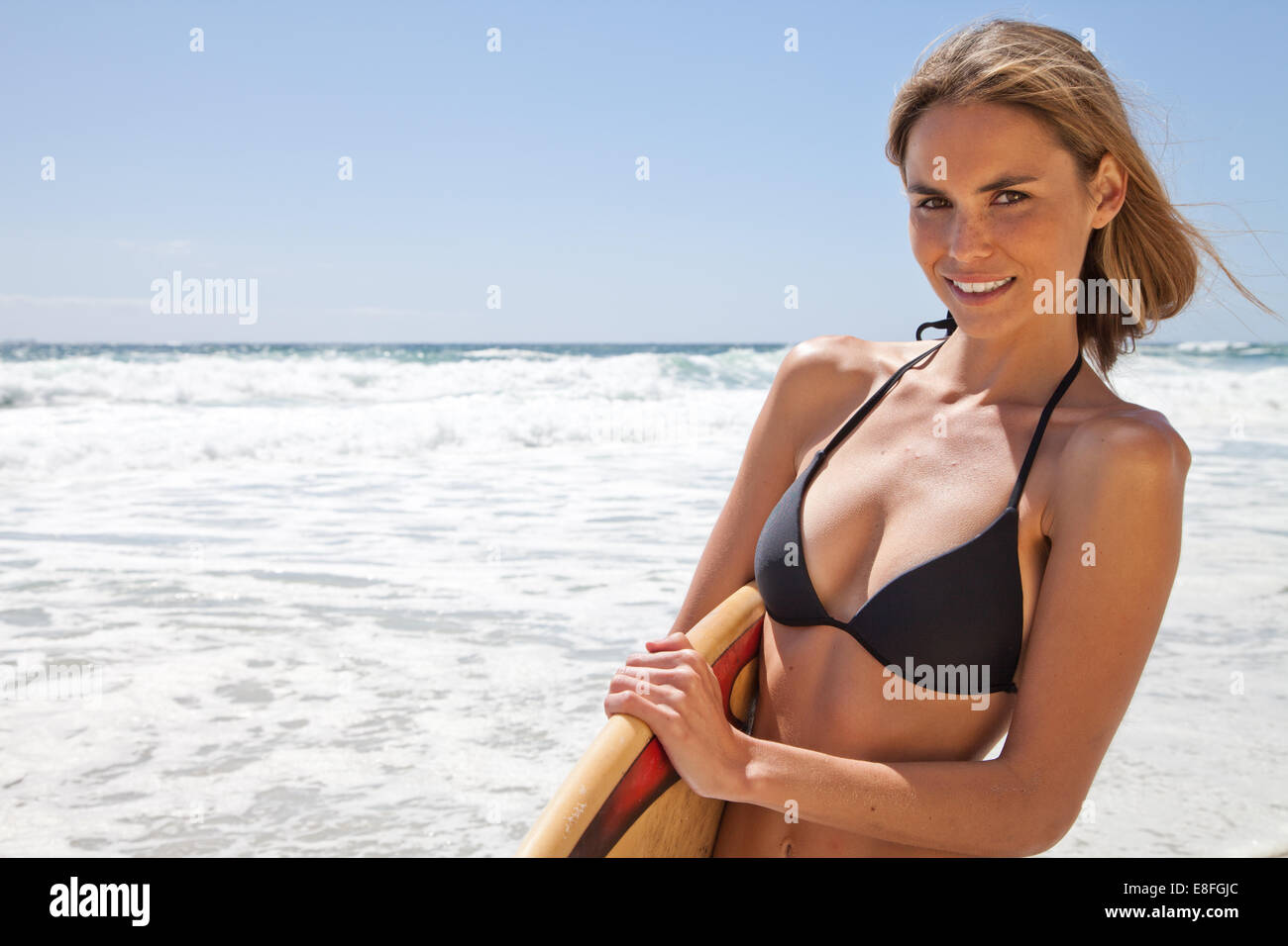 Donna in piedi sulla spiaggia con una tavola da surf, Città del Capo, Capo Occidentale, Sud Africa Foto Stock