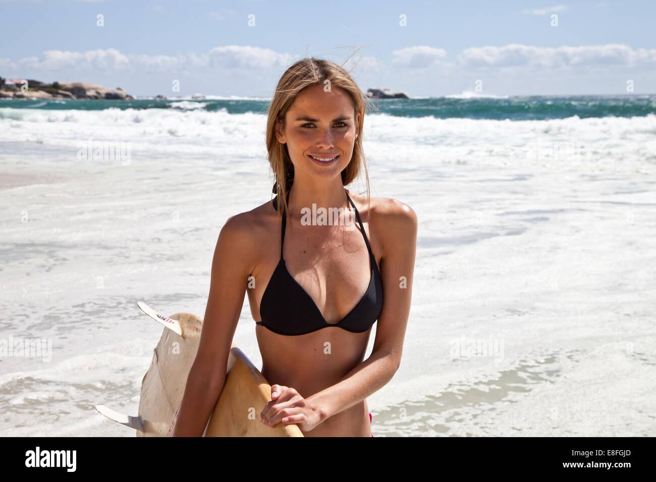 Donna in piedi sulla spiaggia con una tavola da surf, Città del Capo, Capo Occidentale, Sud Africa Foto Stock