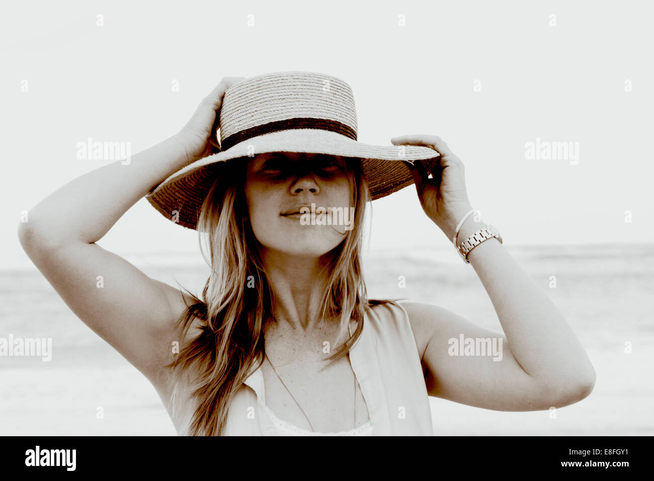 Ritratto di una donna sorridente in piedi sulla spiaggia tenendo il suo cappello, Sudafrica Foto Stock