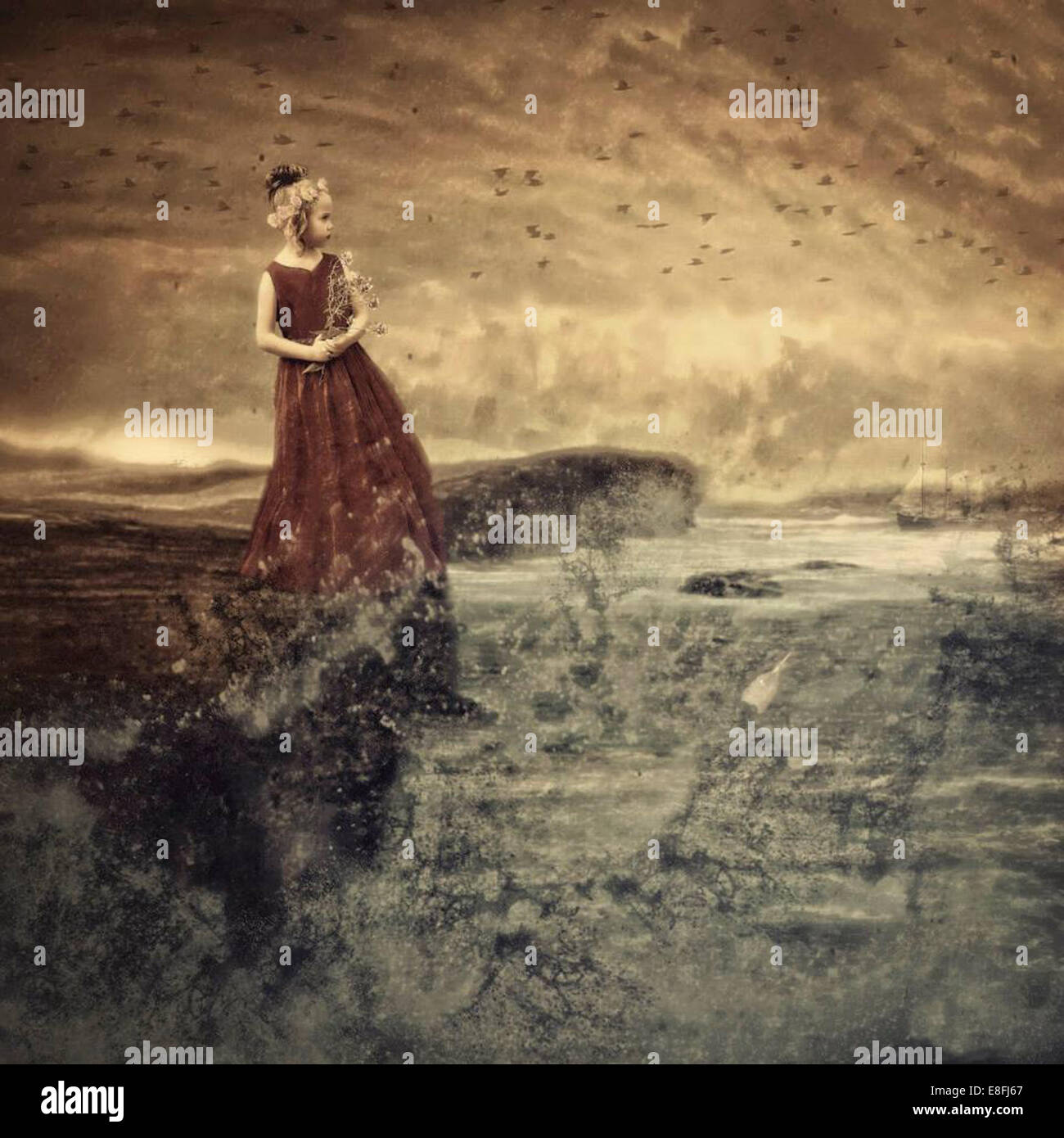 Ragazza vestita come una principessa in piedi su rocce che guardano al mare Foto Stock