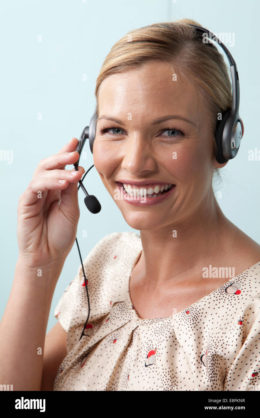 Donna sorridente che parla al telefono utilizzando una cuffia per telefono Foto Stock