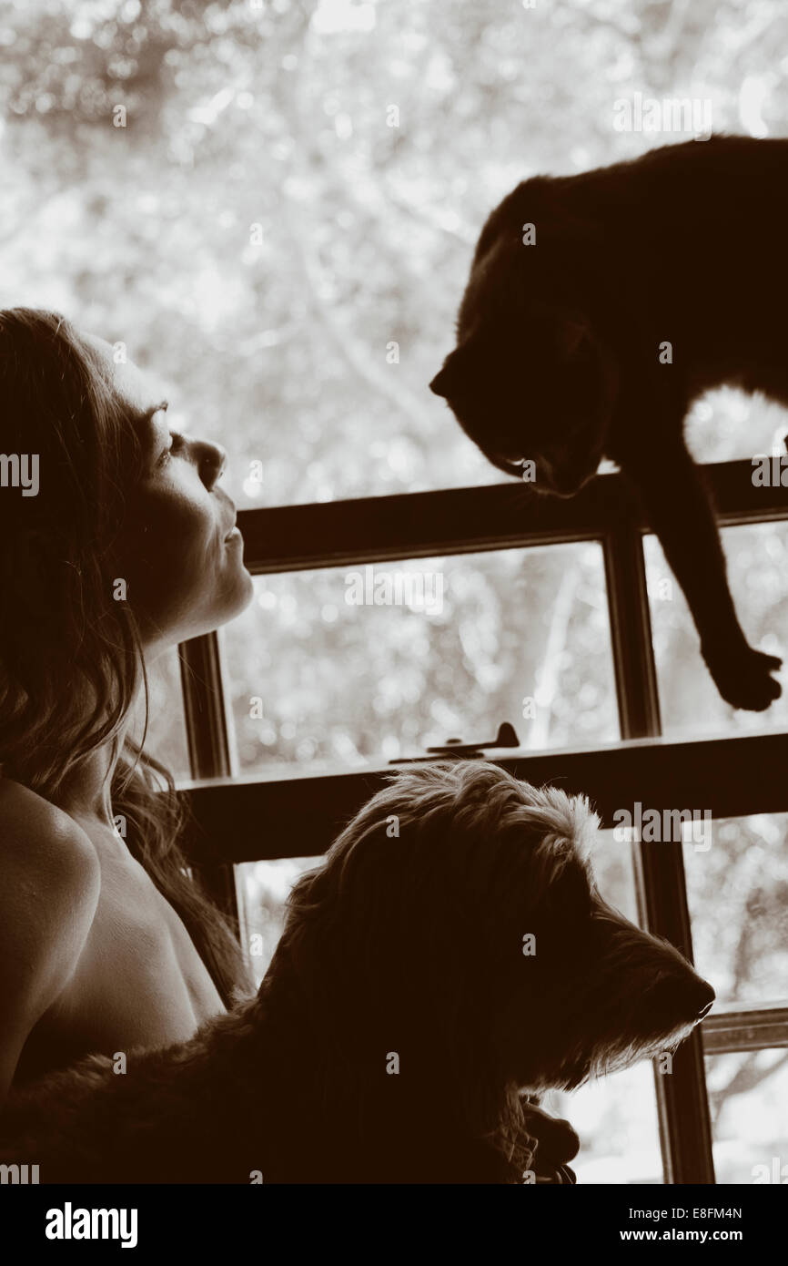 Donna nuda in piedi da una finestra con il suo cane e gatto Foto Stock