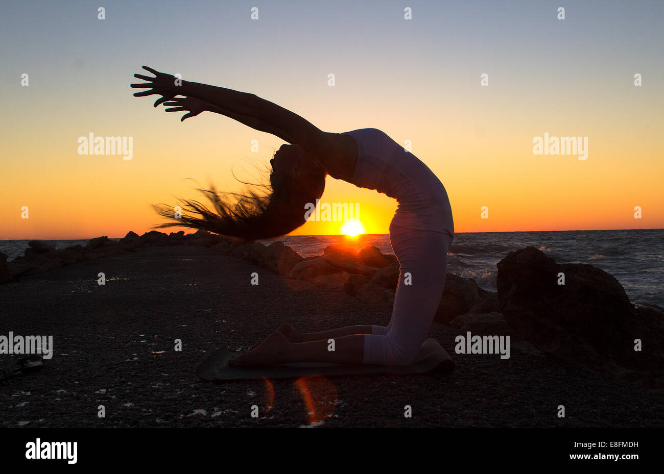 La donna a praticare yoga sulla spiaggia al tramonto Foto Stock