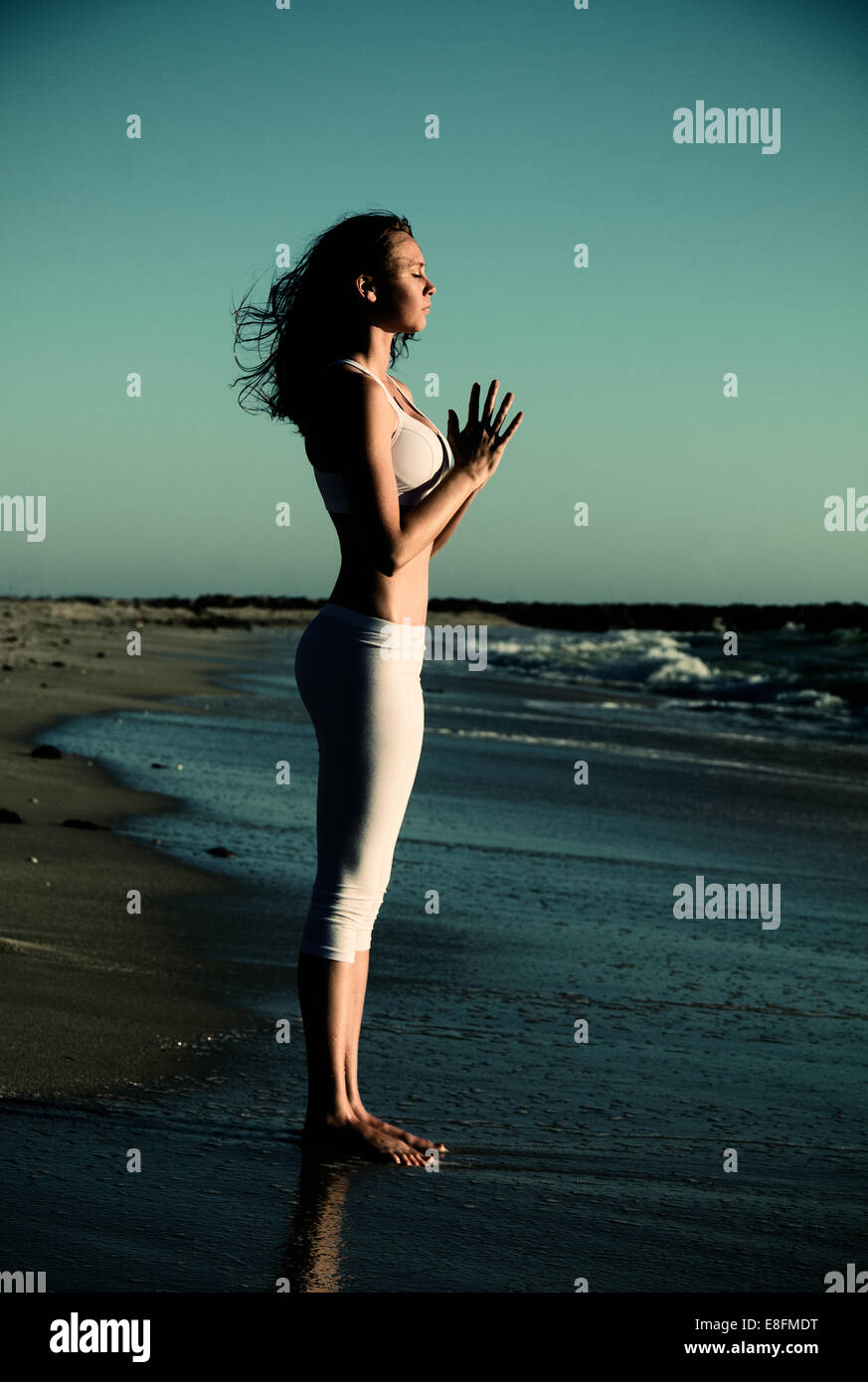 Vista laterale della donna in piedi sulla spiaggia a praticare lo yoga con le mani in posizione di preghiera Foto Stock