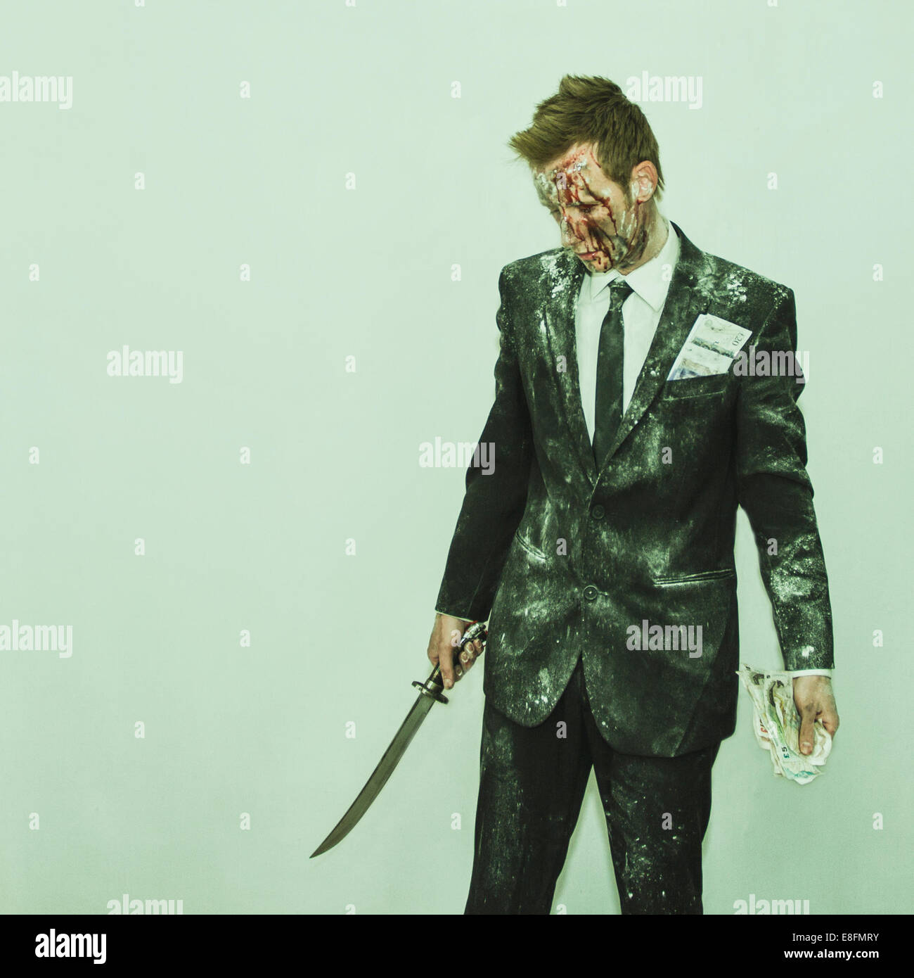 Uomo sanguinato in un vestito sporco con una spada e una manciata di soldi Foto Stock