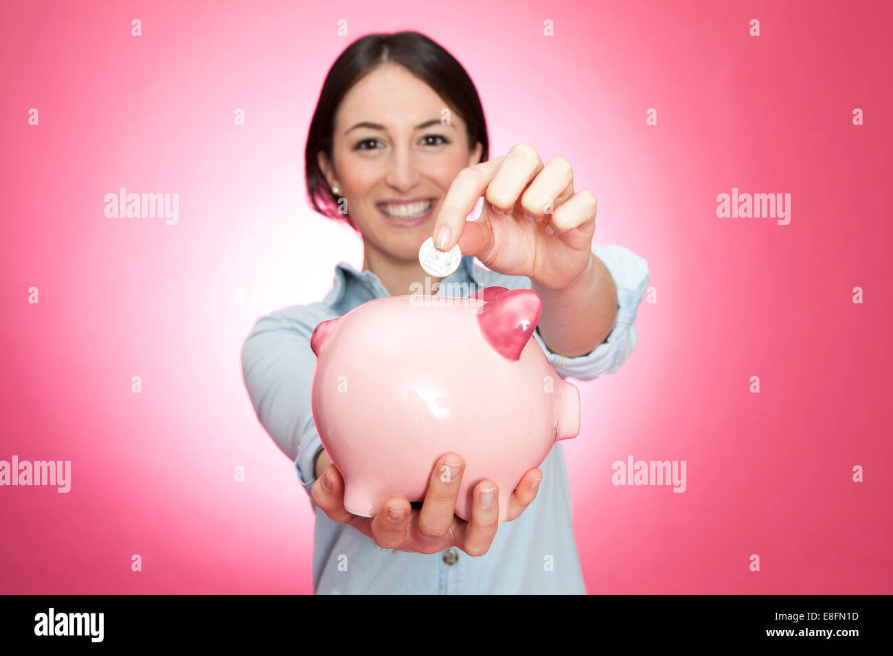 Ritratto di una giovane donna sorridente che inserisce una moneta in una banca piggy Foto Stock