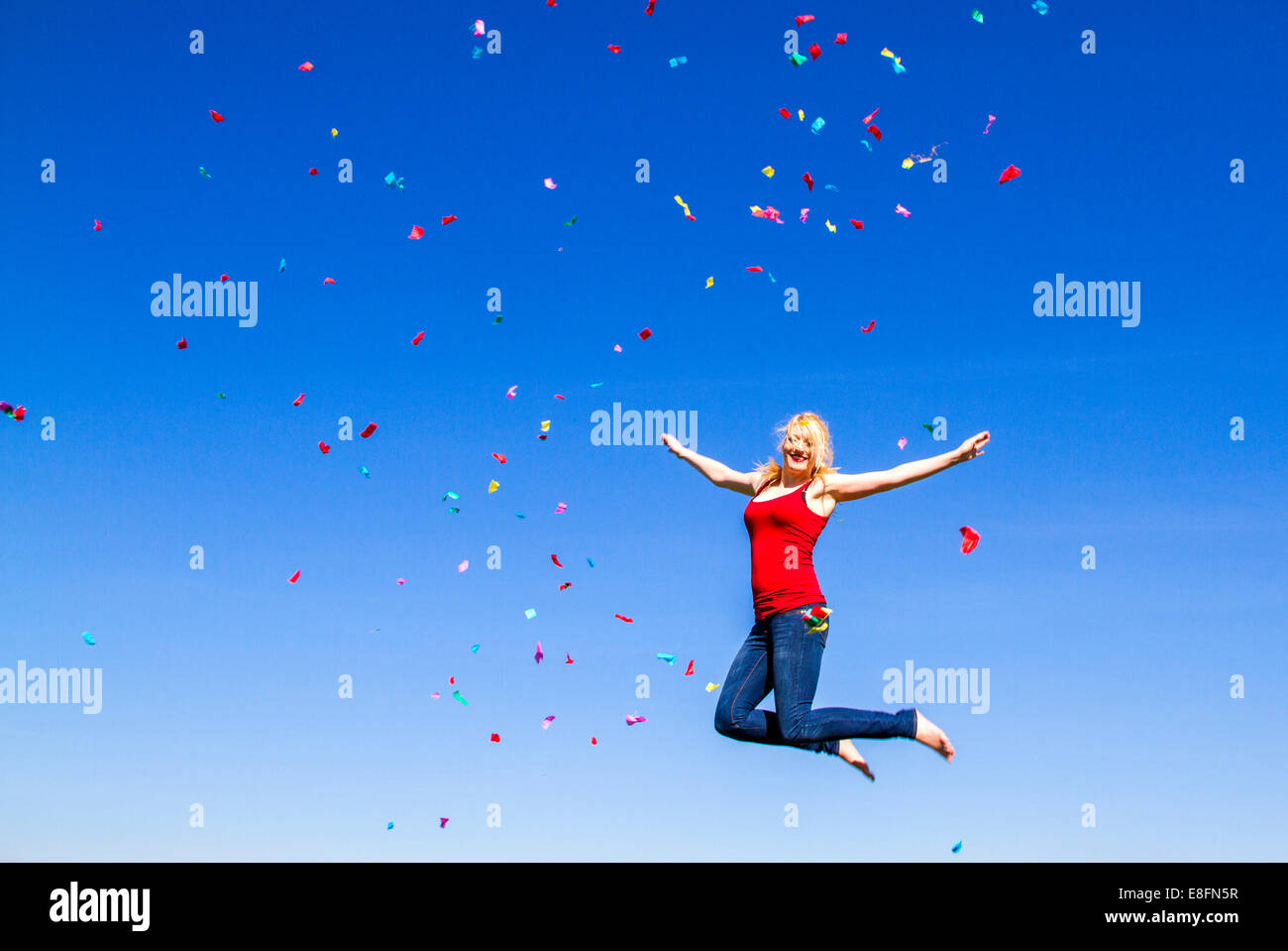 Ritratto di donna bionda jumping con i confetti contro il cielo blu Foto Stock
