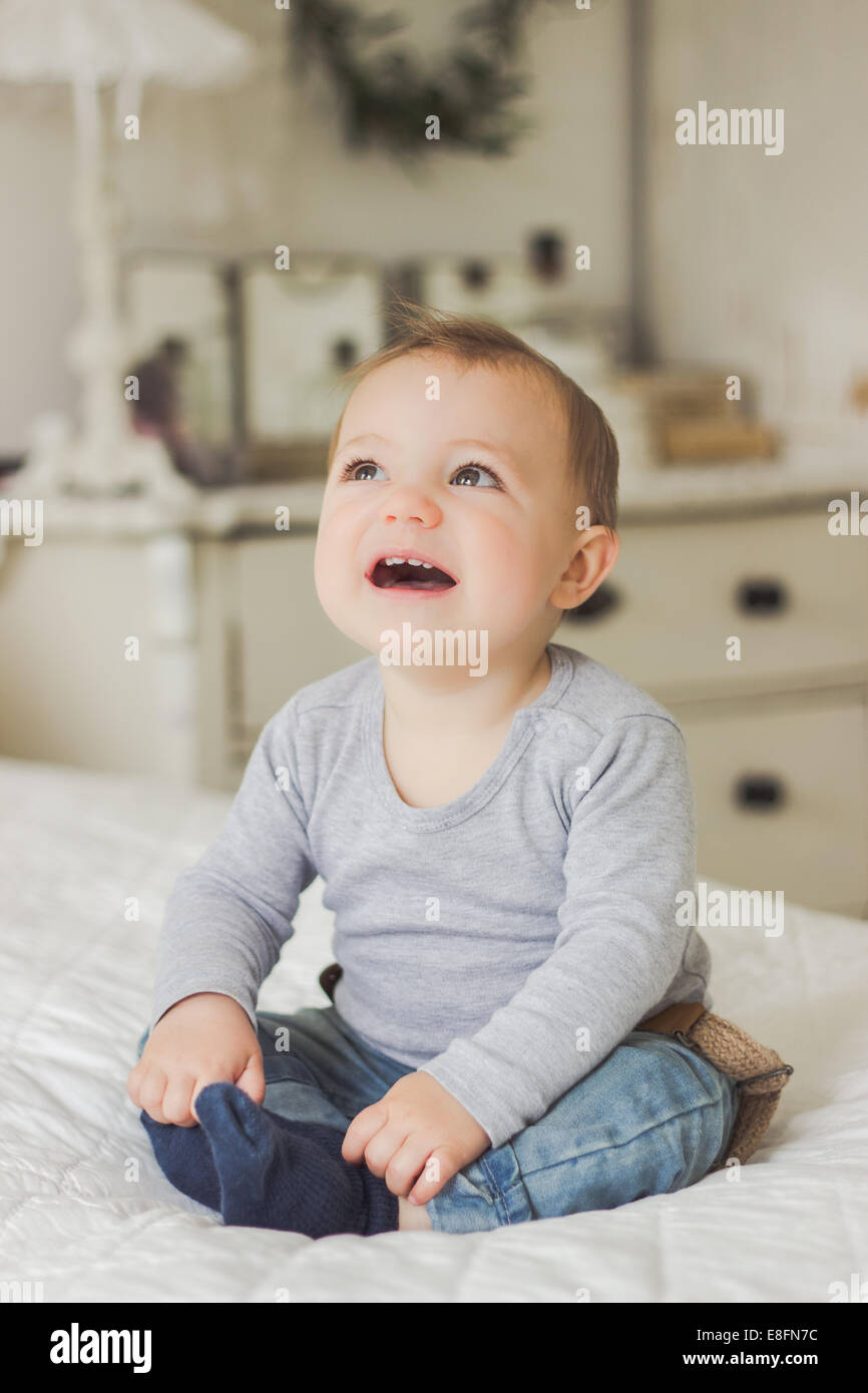 Bambino sorridente seduto su un letto Foto Stock