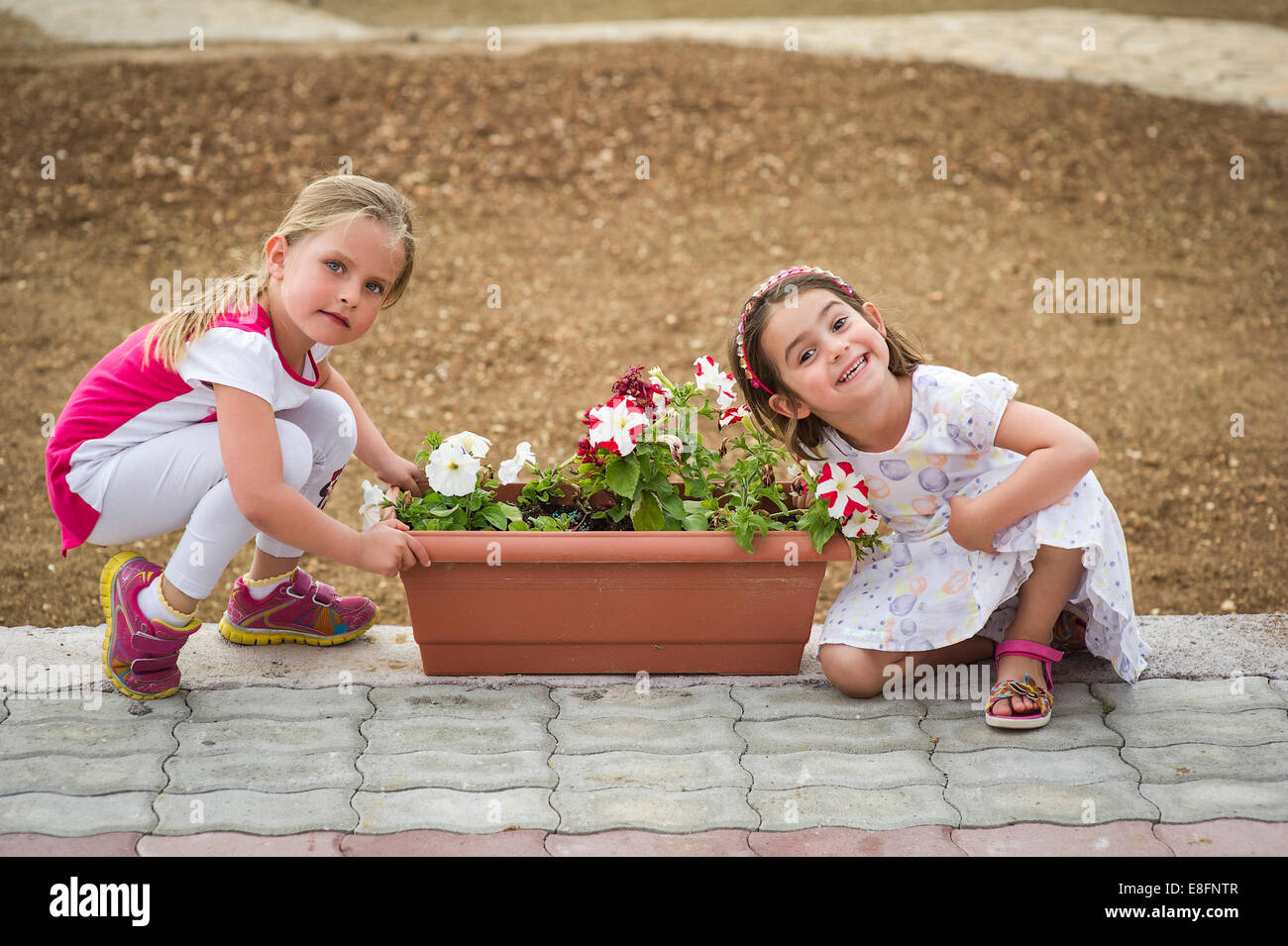 Due ragazze (4-5) per esterni con contenitore per fiori Foto Stock