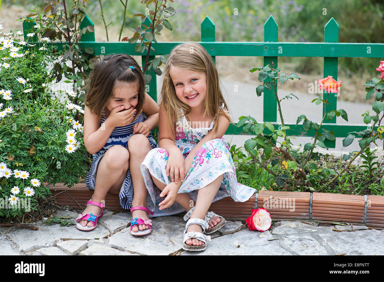 Due ragazze (4-5) seduti all'aperto e ridere Foto Stock
