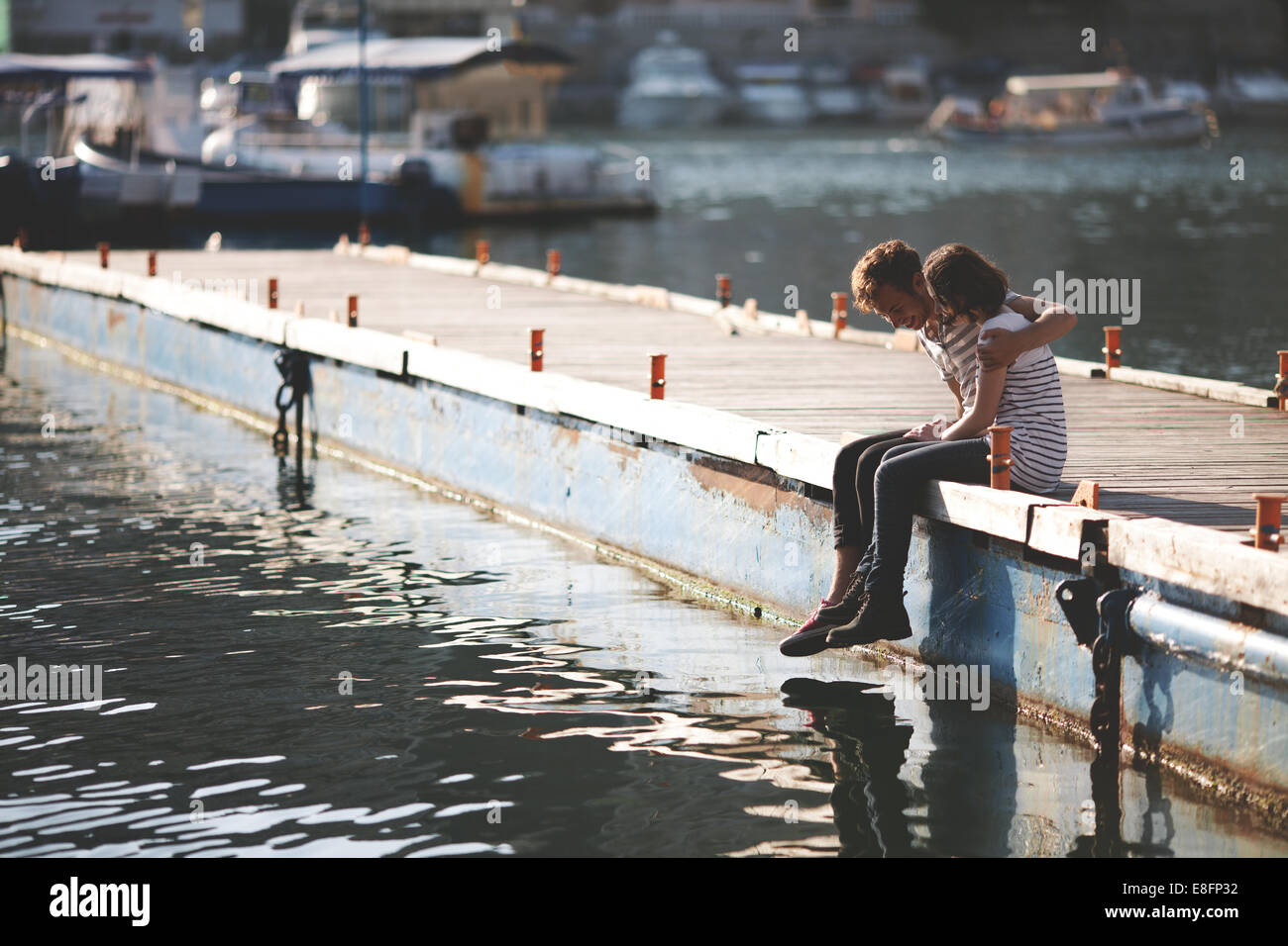 Due adolescenti seduti su un molo con le braccia intorno l'uno all'altro Foto Stock