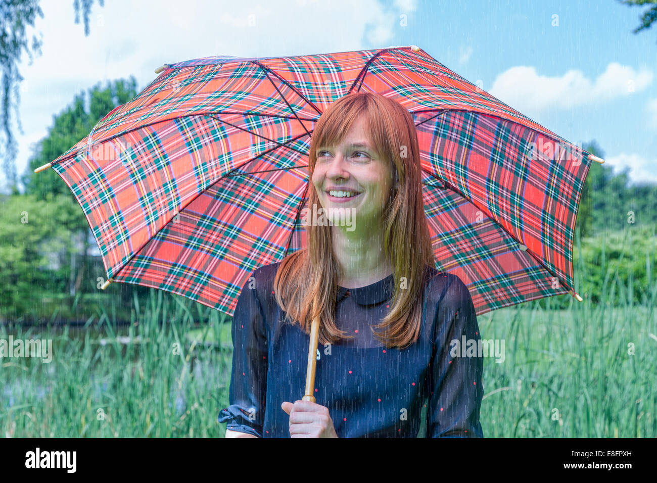 Ragazza con pioggia sotto ombrellone nella natura Foto Stock