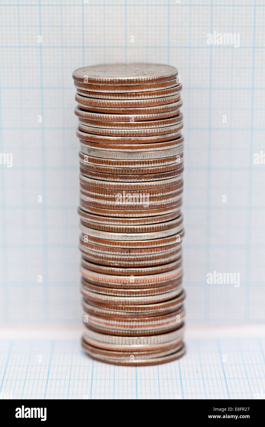 Pila di quarto di dollaro monete accanto a un foglio di carta millimetrata Foto Stock