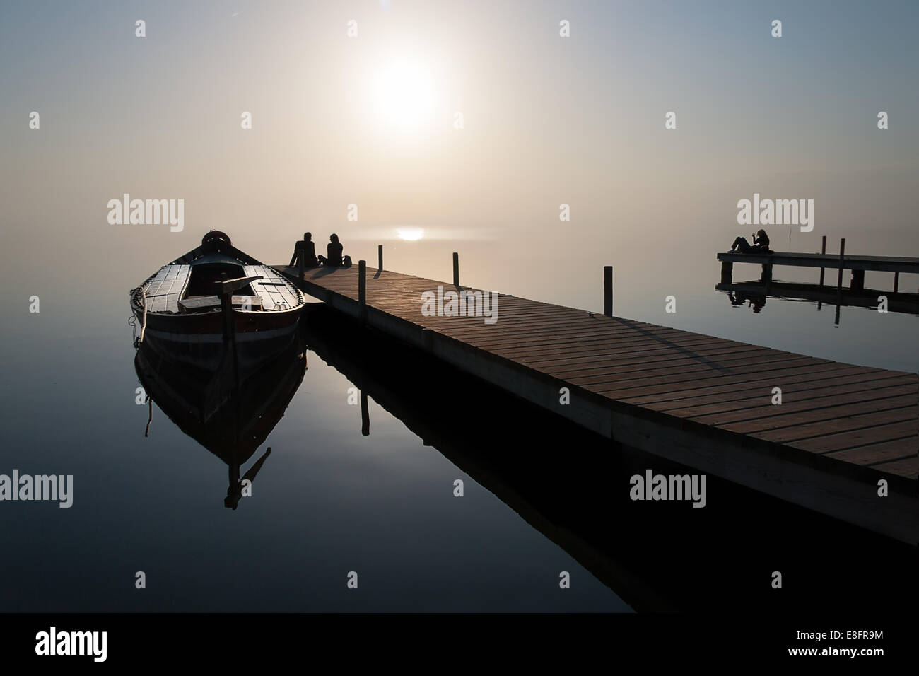 Silhouette di un giovane seduto alla fine del molo dalla barca ormeggiata Foto Stock