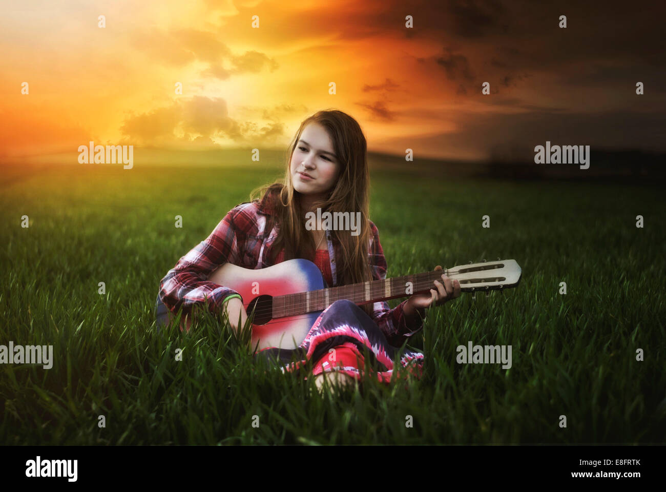 Sorridente ragazza seduta in un prato al tramonto suonando la chitarra, Polonia Foto Stock