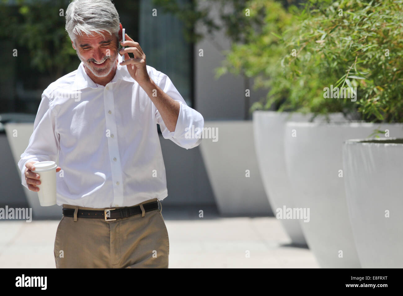 Uomo che parla al telefono tenendo tazza di caffè Foto Stock