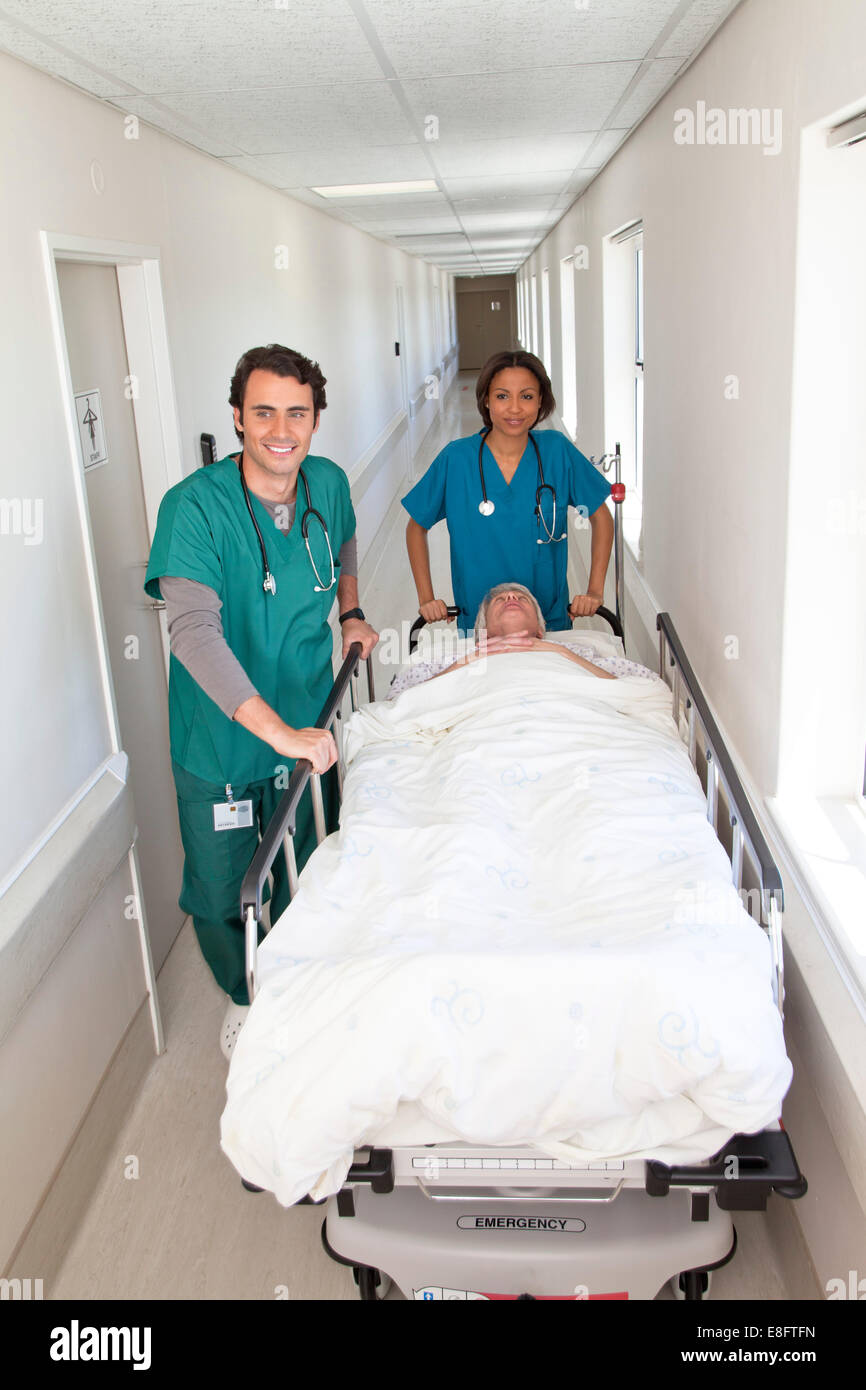 Maschio e femmina in movimento medico paziente sul lettino lungo il corridoio di ospedale Foto Stock