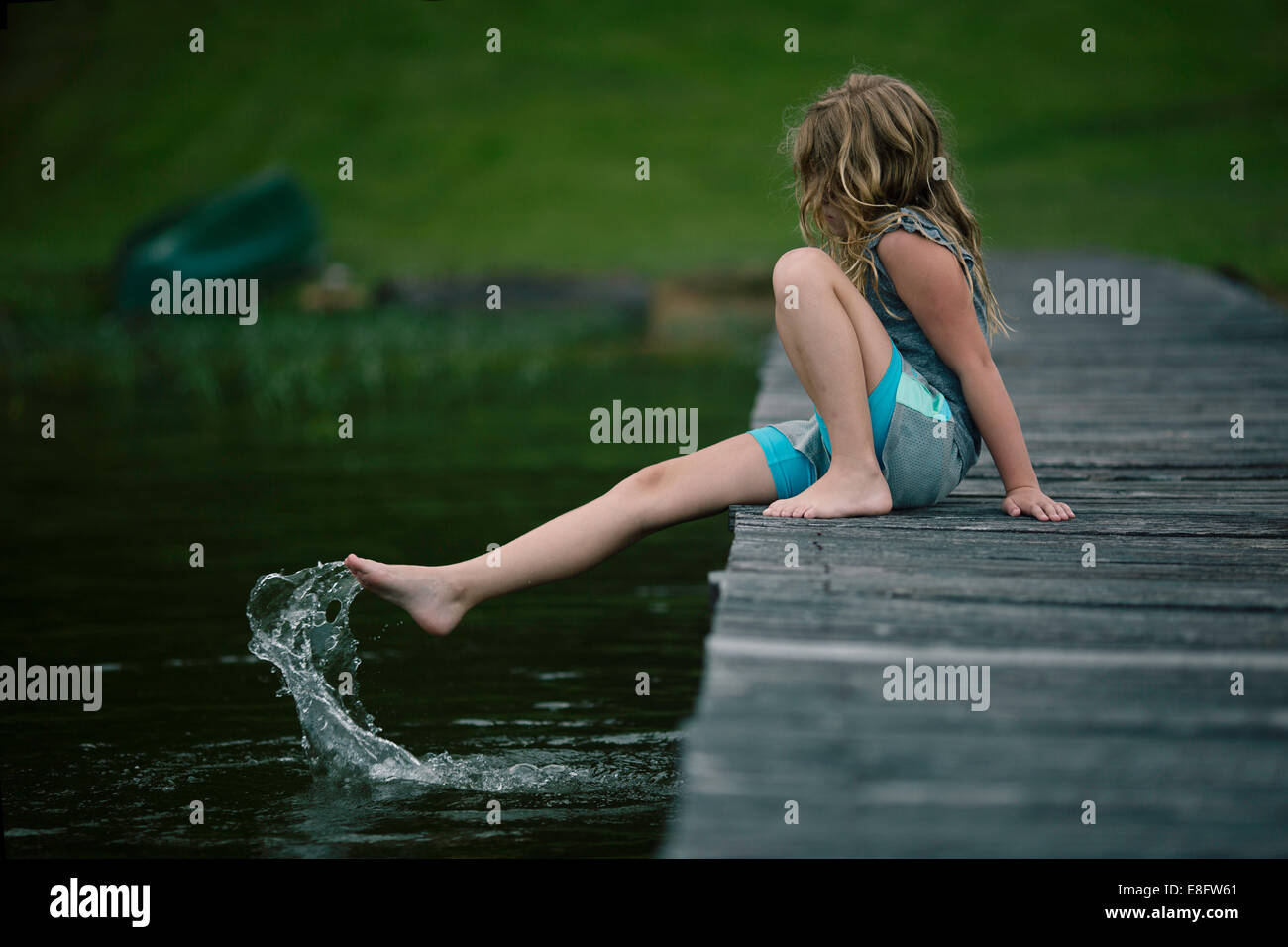 Ragazza seduta sul molo del lago che spruzzi piedi in acqua, Stati Uniti Foto Stock