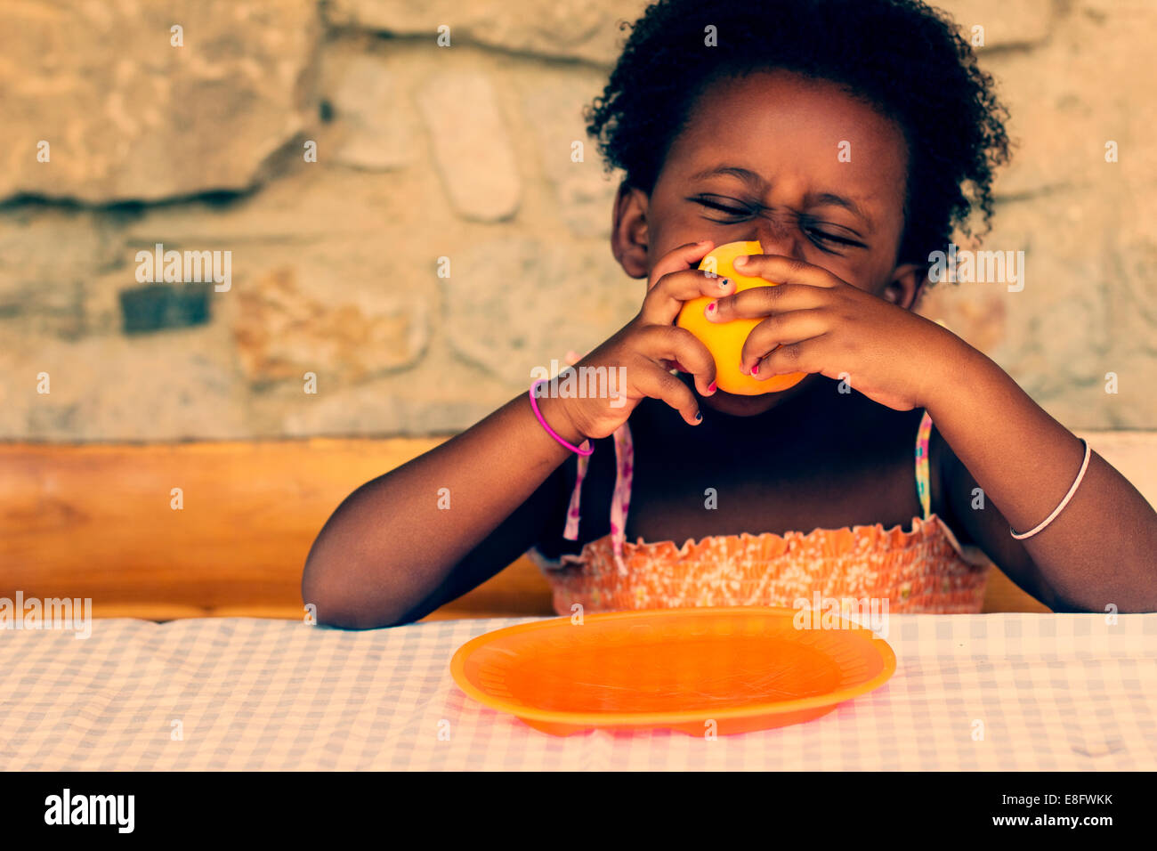 Ragazza seduta a tavola a mangiare un arancio Foto Stock