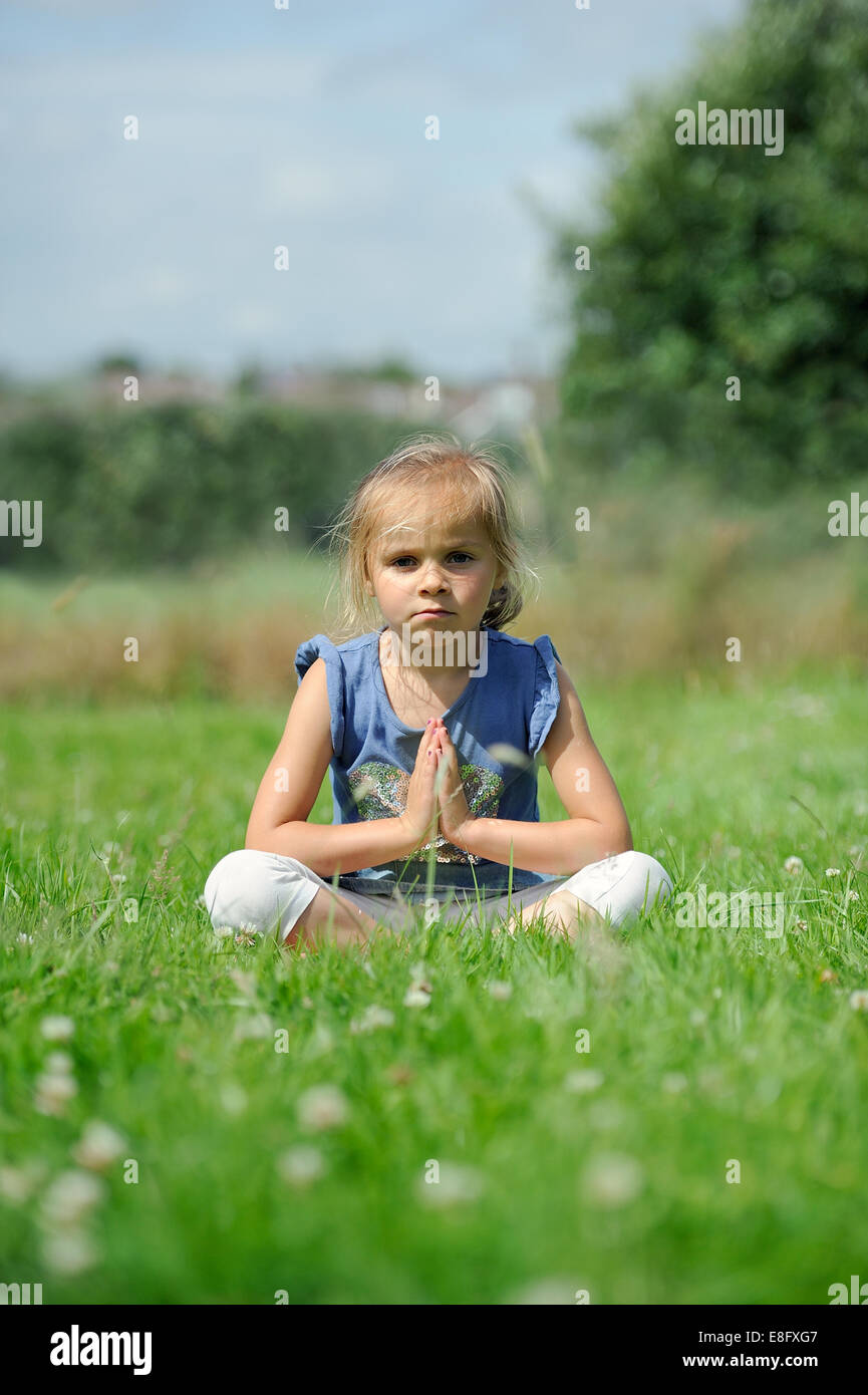 La ragazza (2-3) seduto sull'erba fare yoga Foto Stock