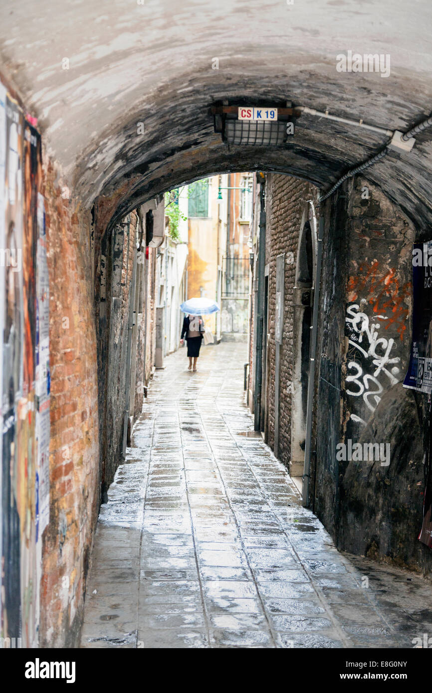 Donna che cammina verso il basso di una Venezia backstreet sotto la pioggia, Venezia, Italia Foto Stock