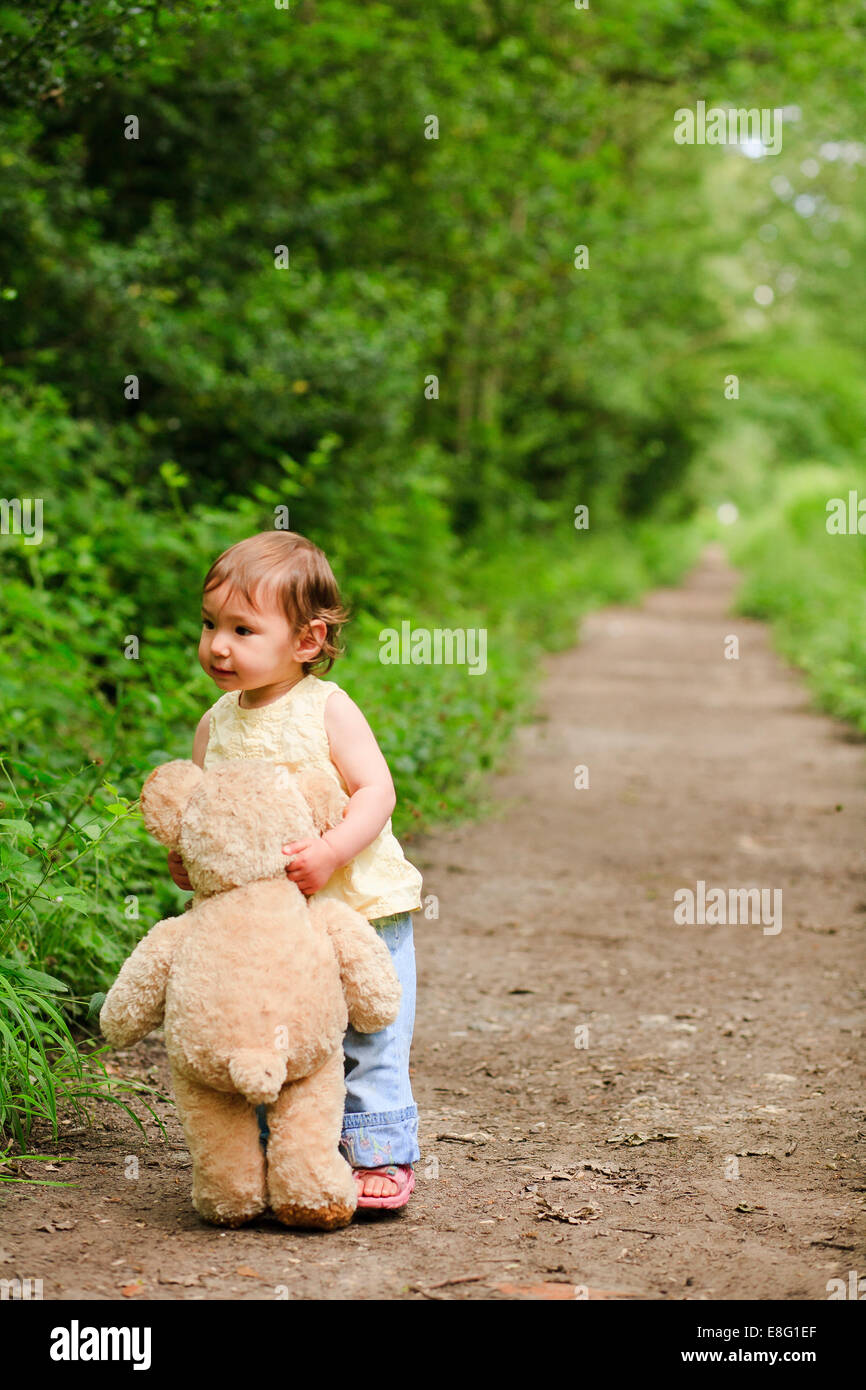 Razza mista asian / toddler caucasica portando il suo orsacchiotto di peluche su una traccia nel bosco Foto Stock
