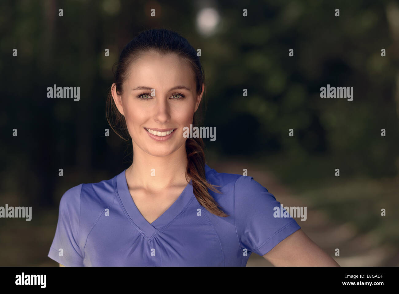 Sorridente attraente giovane donna che indossa una maglietta blu in piedi all'aperto nelle tenebre guardando la telecamera, con spazio di copia Foto Stock