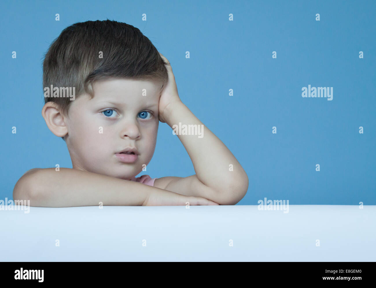 Tre anni carino ragazzo intelligente esprimere emozioni positive in posa sulla parete blu sullo sfondo Foto Stock