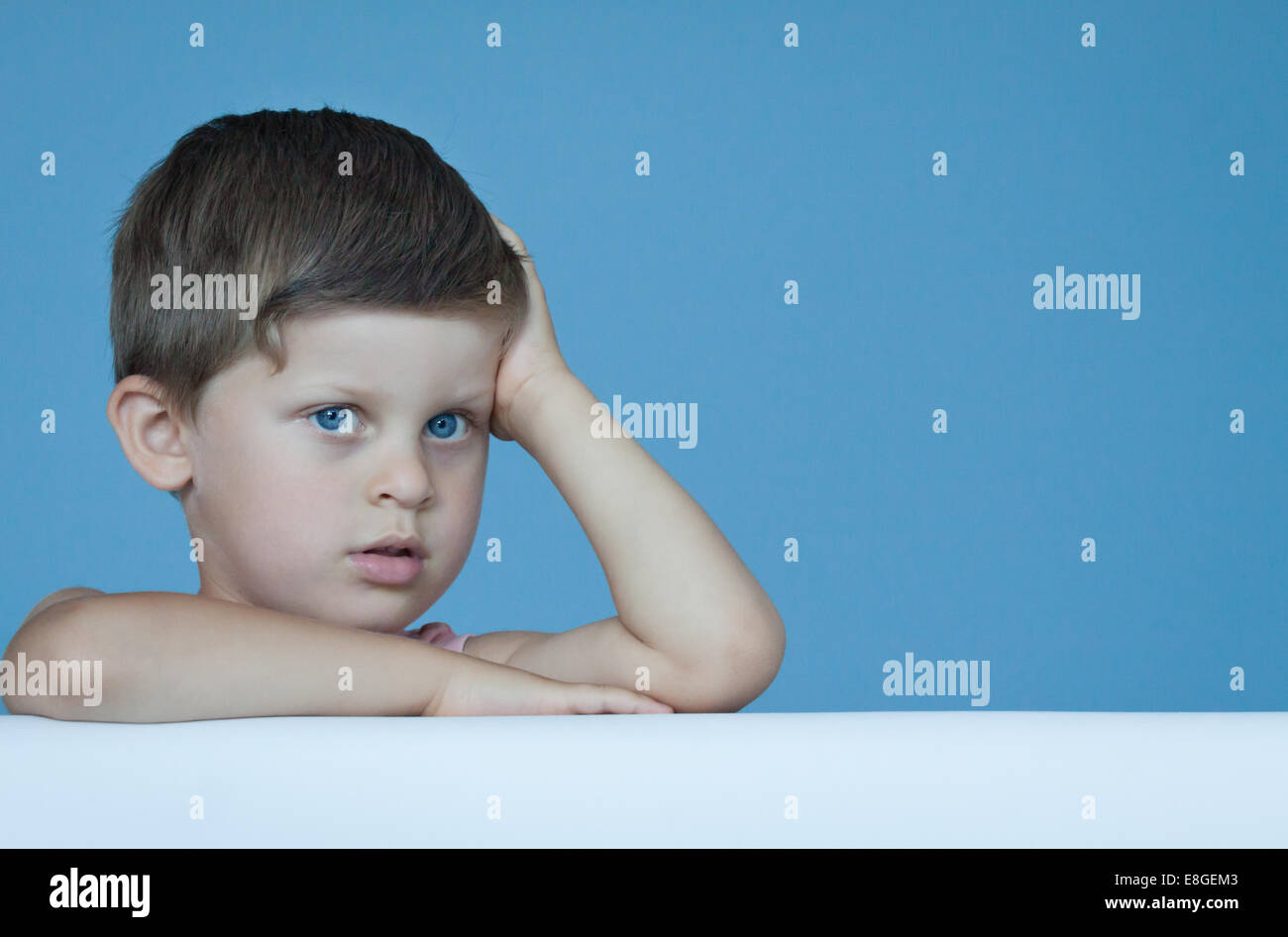 Tre anni giovane ragazzo carino esprimere emozioni positive in posa sulla parete blu sullo sfondo Foto Stock