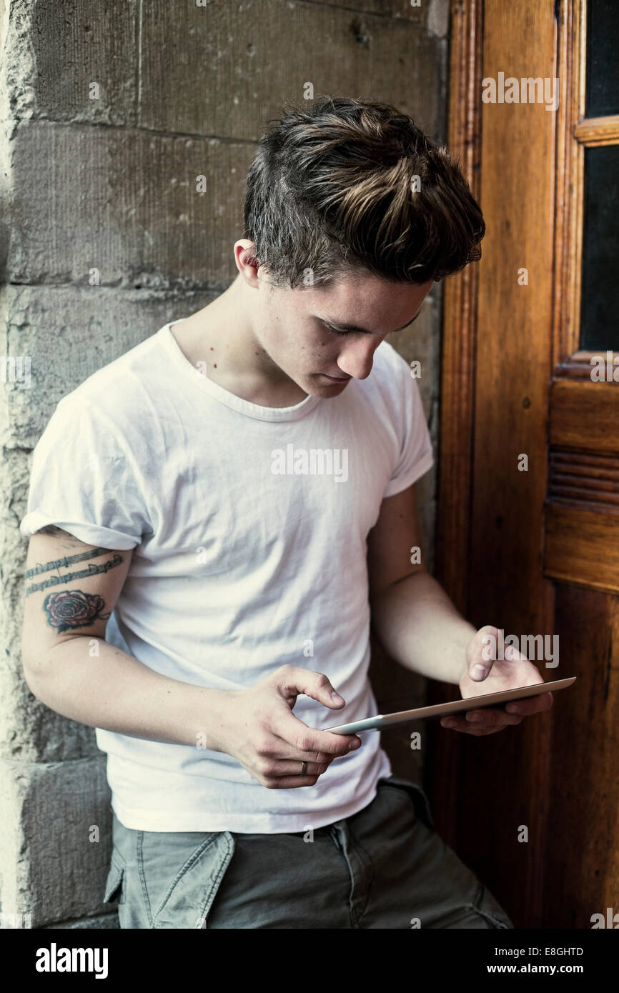 Giovane uomo con tavoletta digitale mentre appoggiata sul alto muro della scuola Foto Stock