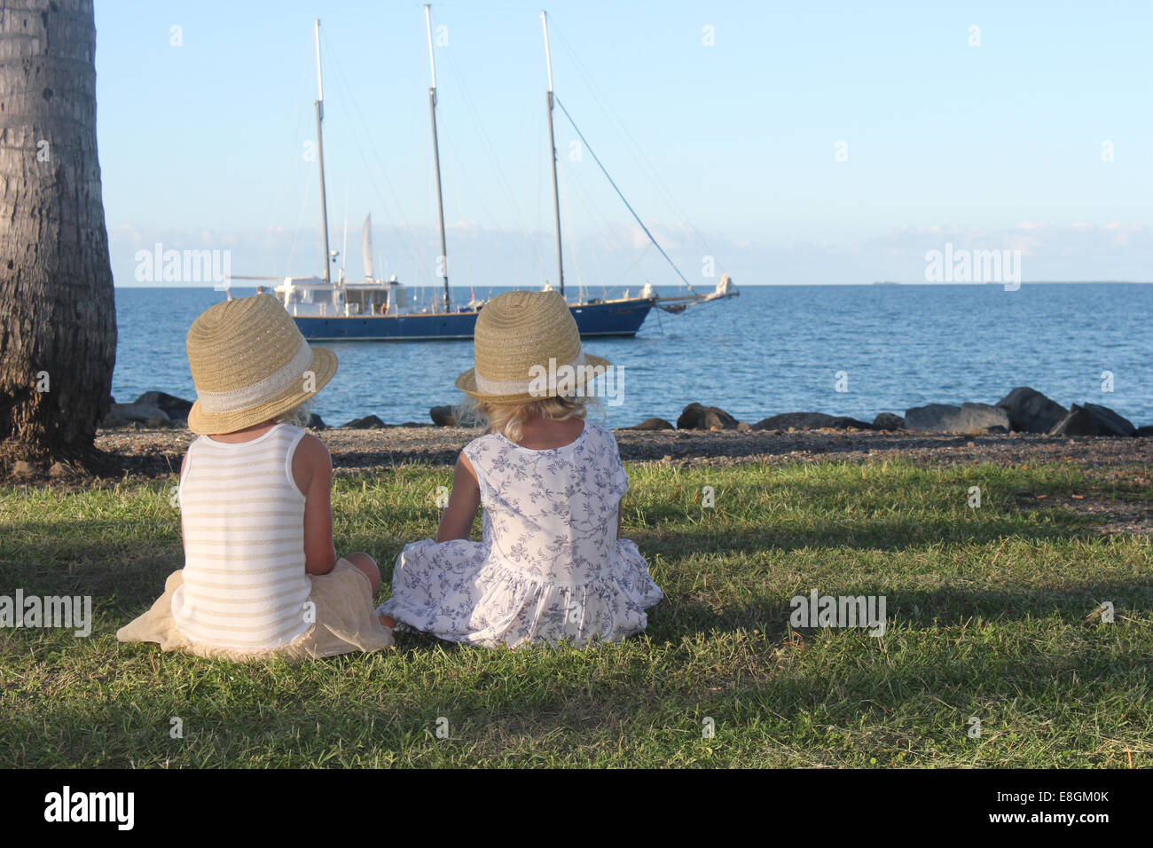 Due ragazze seduto sull'erba guardando barca, Port Douglas, Queensland, Australia Foto Stock