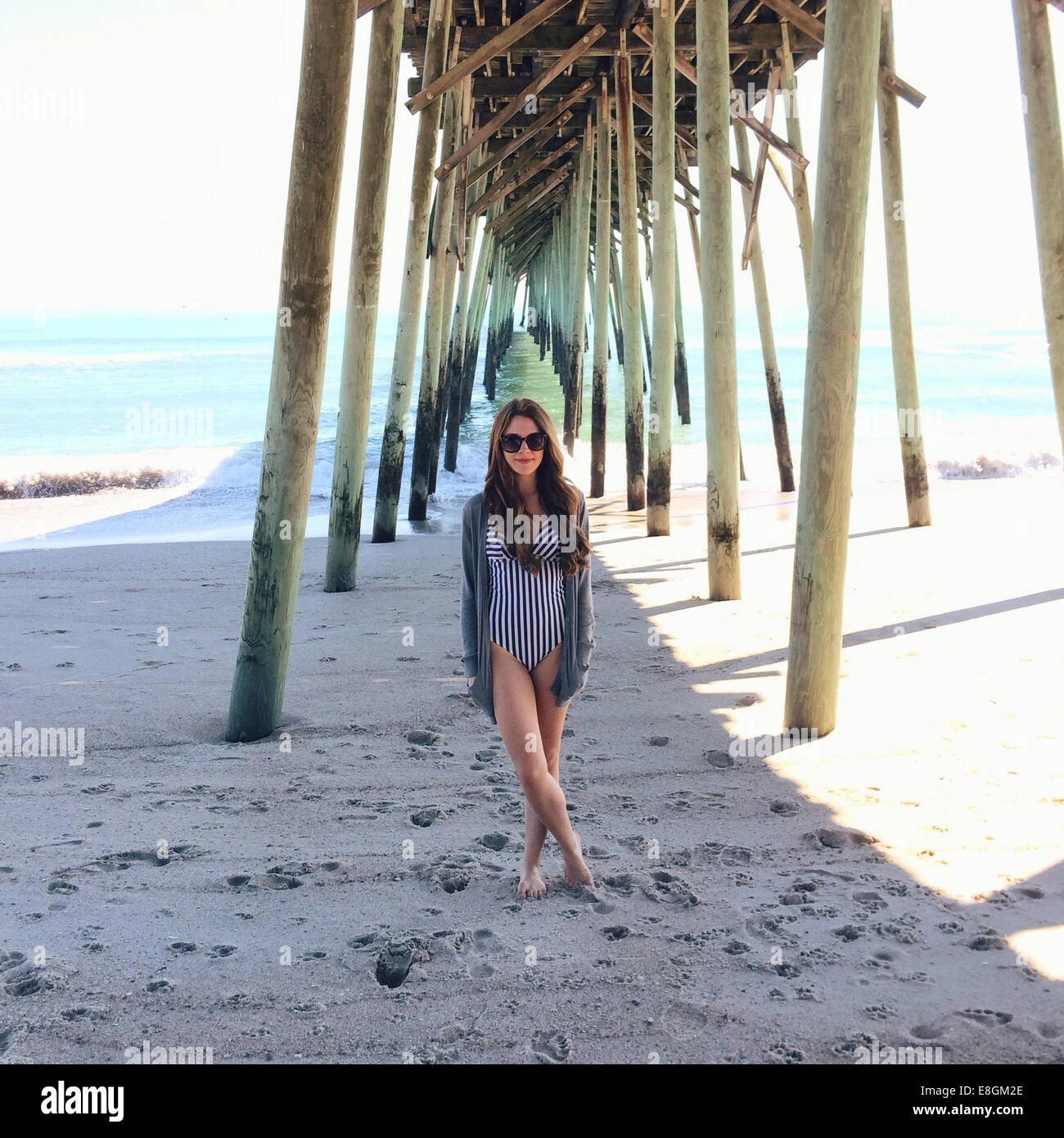 Donna in piedi sulla spiaggia sotto un molo di legno, Carolina Beach, Carolina del Nord, Stati Uniti Foto Stock