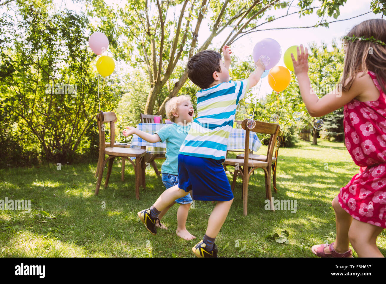 I bambini cercando di catturare le bolle di sapone in giardino Foto Stock
