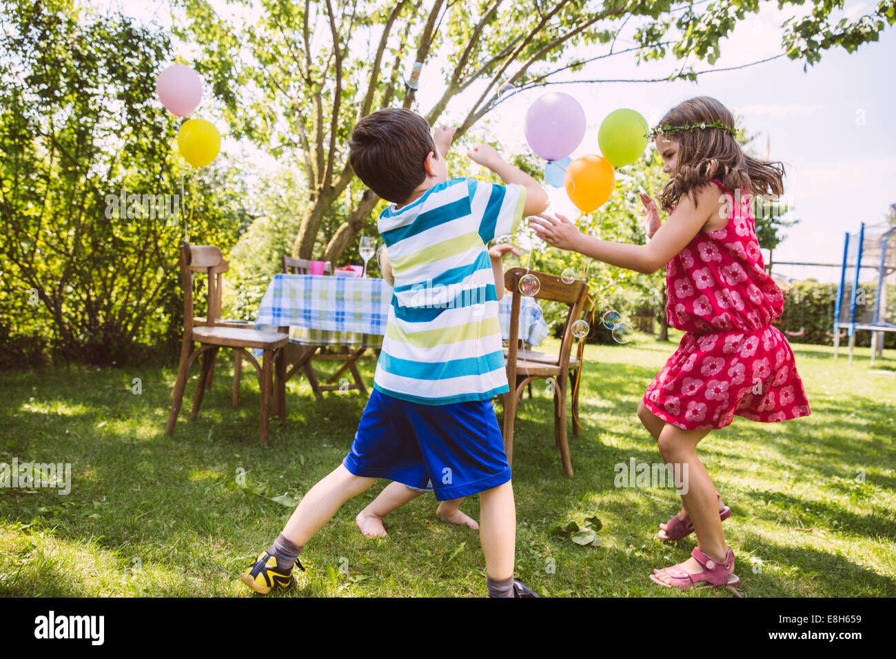 I bambini cercando di catturare le bolle di sapone in giardino Foto Stock