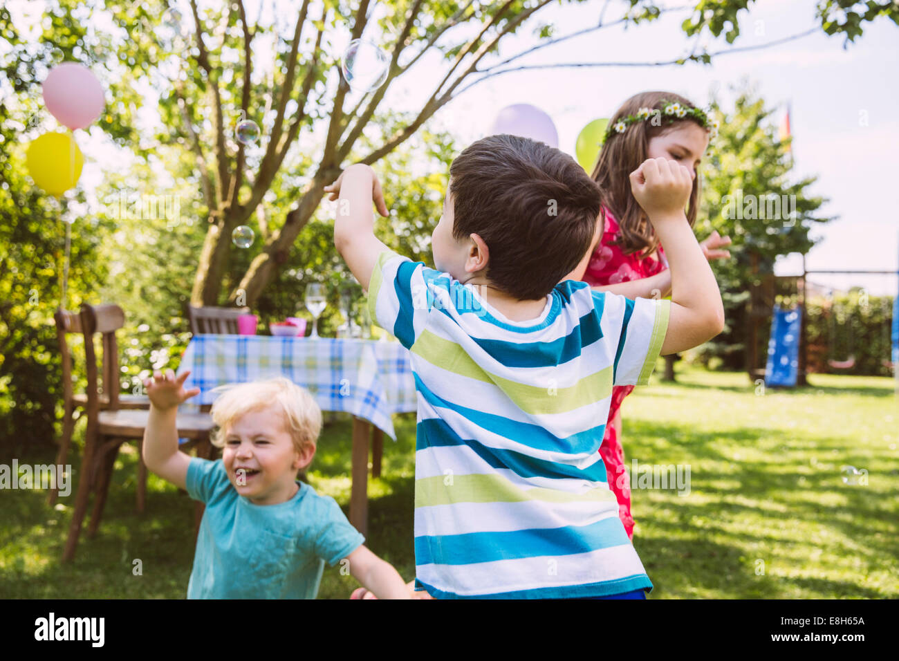 I bambini cercando di catturare le bolle di sapone in giardino Foto Stock