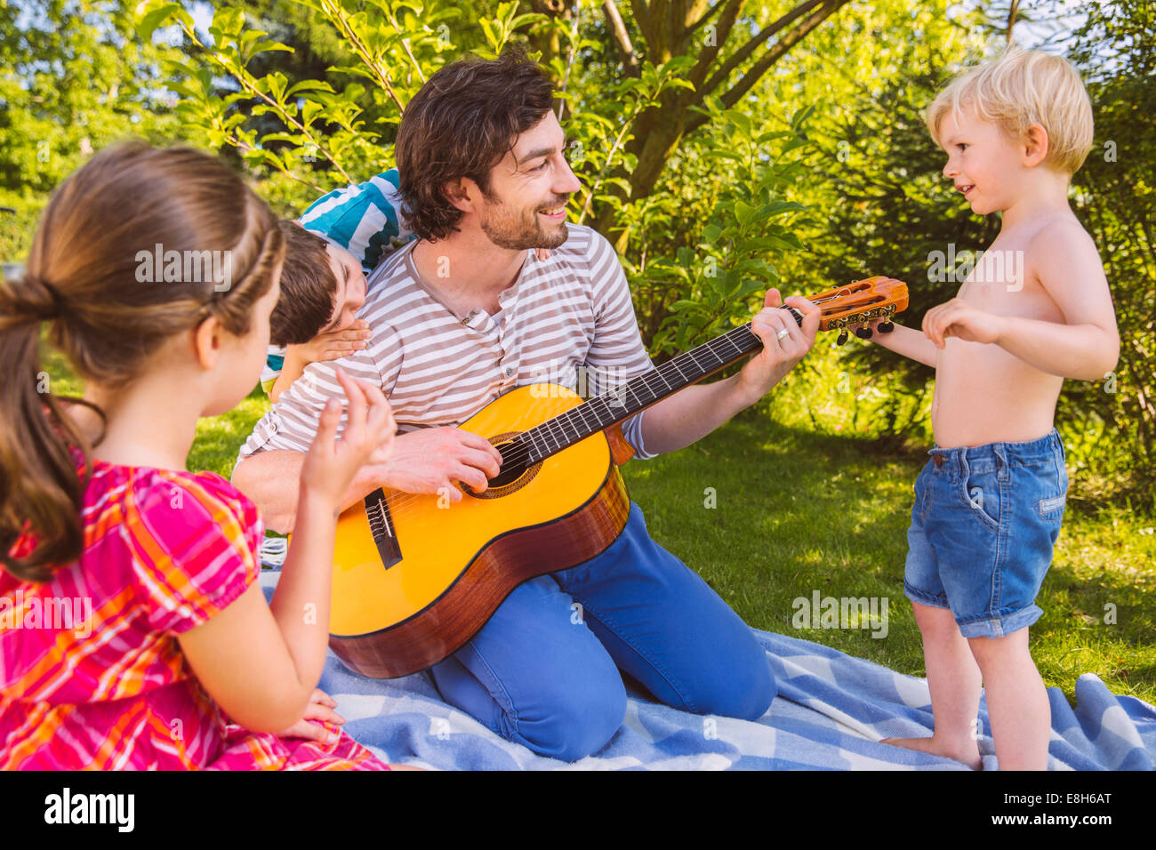 Padre con i bambini a suonare la chitarra in giardino Foto Stock