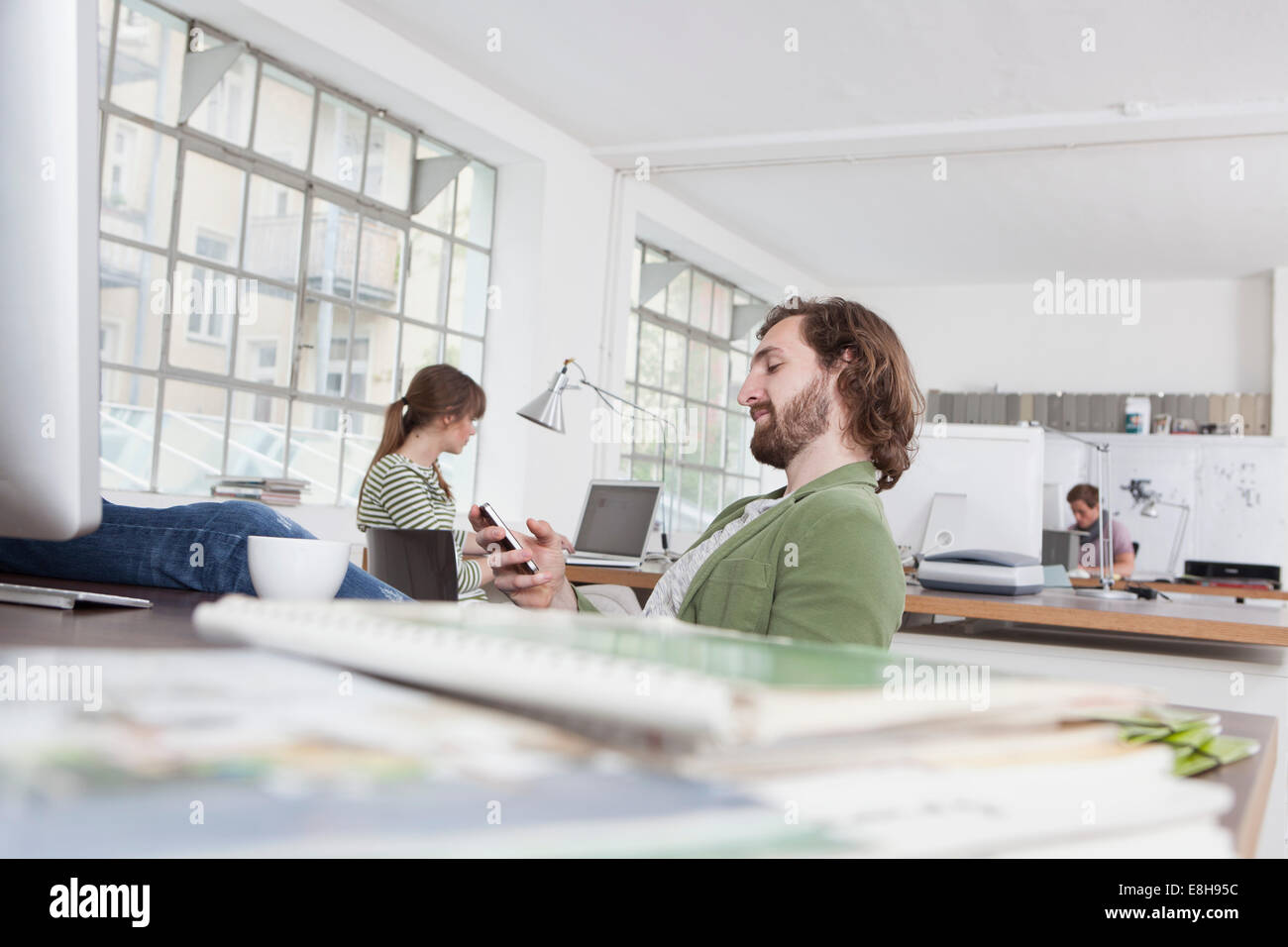 Giovane uomo seduto alla sua scrivania in un ufficio creativo utilizzando il suo smartphone Foto Stock